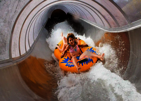 Zwei Kinder fahren auf einem gelben Doppelreifen durch eine Kurve im geschlossenen Speed Blaster.