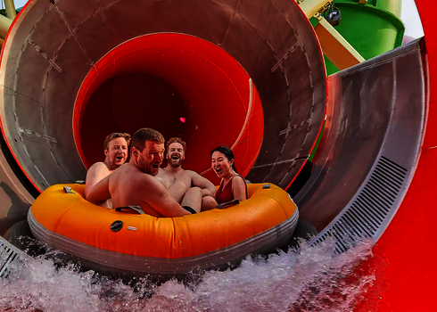 Vier Erwachsene fahren im gelben Reifen aus dem roten Tunnel der Reifenrutsche RR2700 heraus.