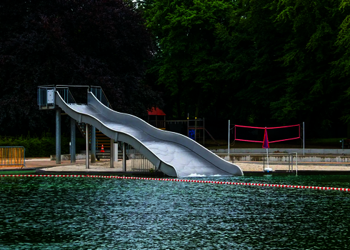 Breitwellenrutsche auf Edelstahlstützen an einem Badesee, im Hintergrund ein Volleyballfeld.