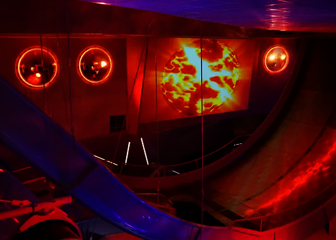 Teilansicht einer Boomerang Wasserrutsche mit roter und lila Beleuchtung in einem Hallenbad.