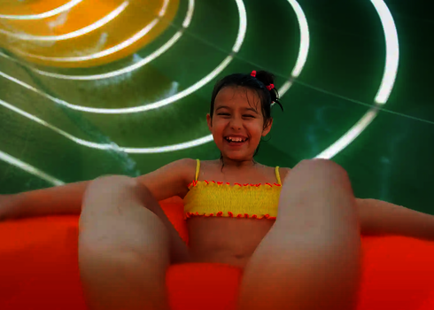 Ein Mädchen fährt lachend in einem orangen Reifen durch die grün-gelb beleuchtete Family Twister Rutsche.