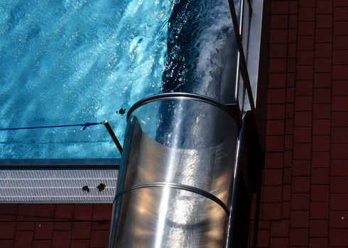 Blich von oben auf den Auslauf einer Wasserrutsche, die in ein Schwimmbecken mündet.