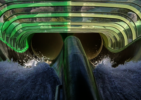 Blick auf die grüne Raft Racer Wasserrutsche mit transparenten Abschnitten und Wasserspritzern.