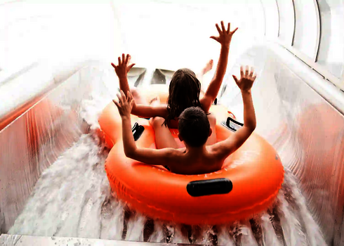 Zwei Kinder rutschen mit erhobenen in orangem Doppelreifen durch die Raft Racer Wasserrutsche.