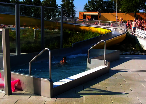 Yellow slide with water basin in an outdoor swimming pool, a child is swimming in the pool.
