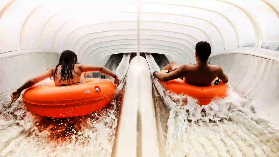 Zwei Personen fahren nebeneinander mit orangen Reifen in der Raft Racer Reifenrutsche.