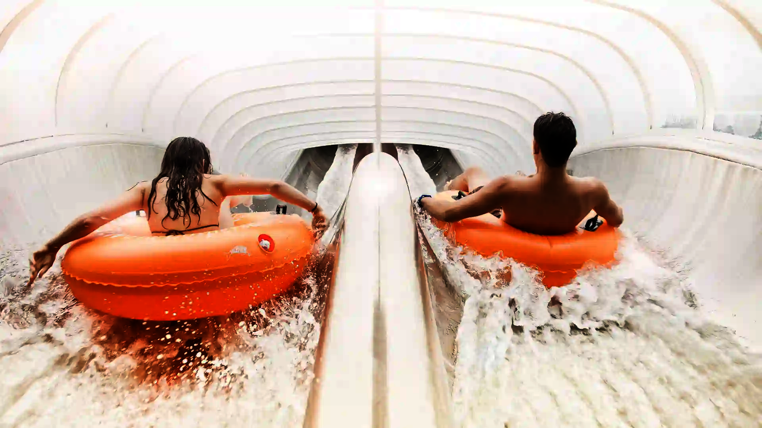 Zwei Personen fahren nebeneinander mit orangen Reifen in der Raft Racer Reifenrutsche.