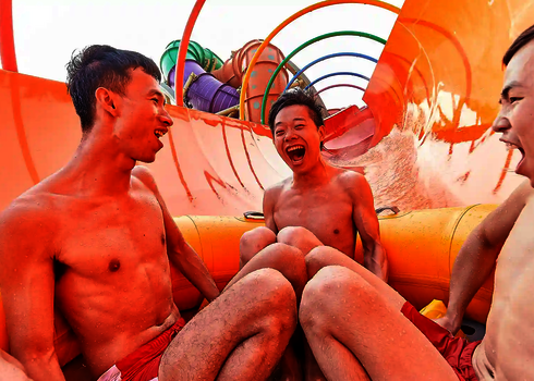 Drei Männer rutschen lachend durch den orangenen Tunnel mit bunten Regenbogenringen der RR2700.