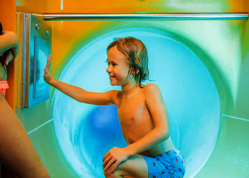 Kind drückt Hand auf einen Bildschirm im türkisfarbenen Startbereich einer Wasserrutsche.