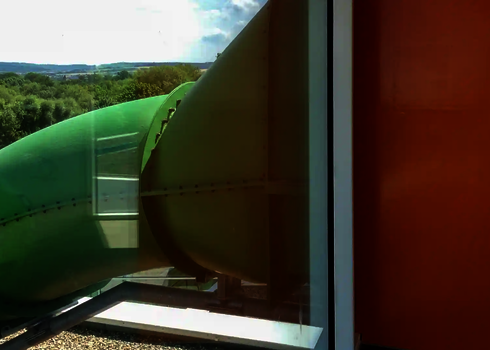 Blick auf grüne Wasserrutsche, die durch die Glasfassade eines Gebäudes nach draußen führt.