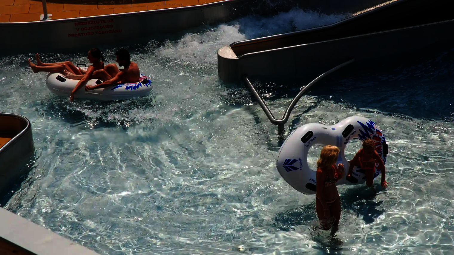 Zwei Kinder und ein Paar nutzen den Lazy River mit Rutschreifen.