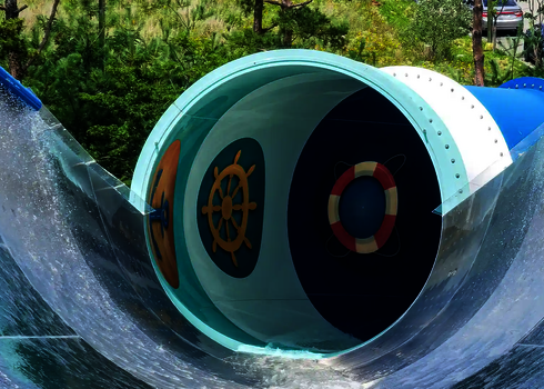 Innenansicht der Rutsche mit großen Tageslichtmotiven: Steuerrad, Rettungsring und Anker leuchten durch.