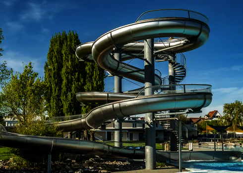Mehrere Edelstahlrutschen verlaufen spiralförmig an einem Rutschenturm in einem Freibad.