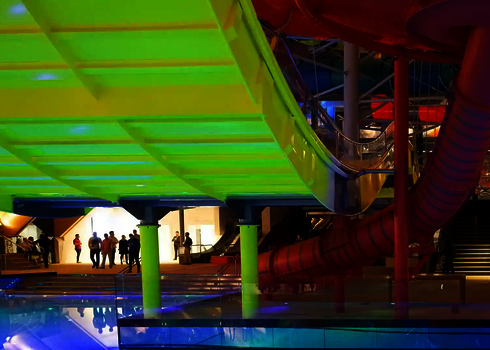 Grün leuchtende Unterseite der Boomerang-Rutsche über dem Innenpool, Personen im Hintergrund.