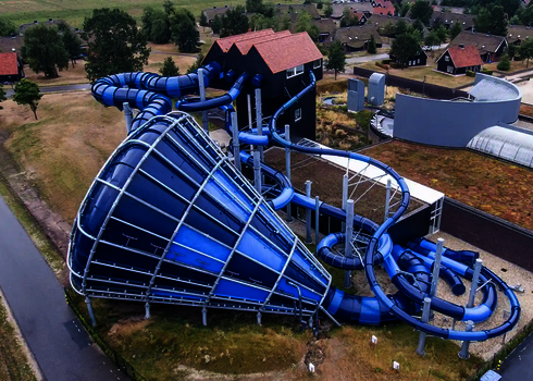 Blauer Cyclone-Trichter mit weit verzweigter Röhrenrutsche in Landschaft mit Ferienhäusern.