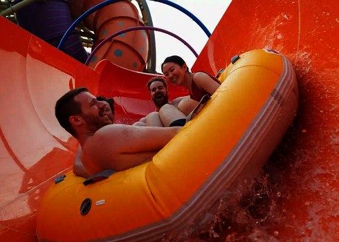 Vier Erwachsene rutschen gemeinsam im gelben Reifen durch die bunte RR2700 mit Regenbogenelementen.