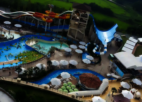 Blick auf einen Wasserpark mit einem blauen Urknall, Schwimmbecken mit vielen gelben Rutschreifen.