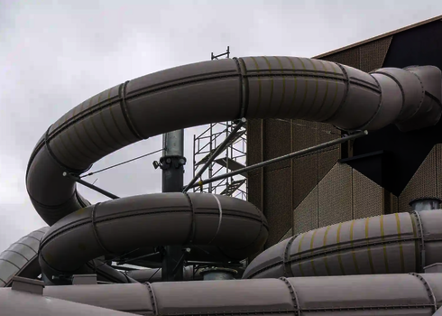 Mehrere gedämmte Röhrenrutschen verlaufen um einen zentralen Träger an einem Gebäudekomplex.