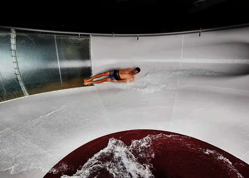 Eine Person in Badebekleidung rutscht in einer weißen Body Bowl Wasserrutsche.