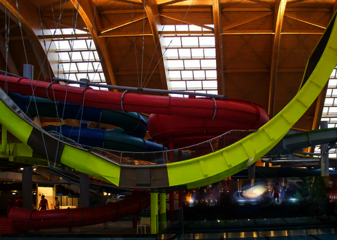 Indoor-Boomerang-Rutsche mit gelber Trägerstruktur, umgeben von Spiralrutschen.