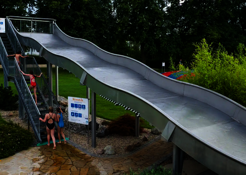 Wasserrutsche auf Stahlstützen und mit einer Treppe auf der sich Personen befinden.