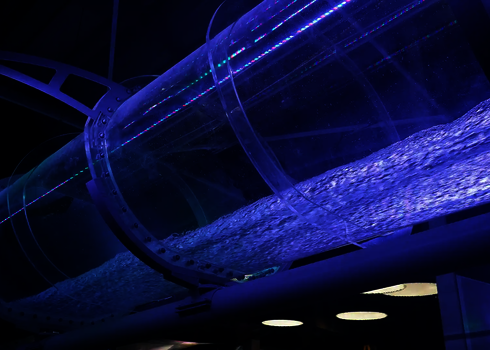 Transparente Rutsche mit LED-Lichteffekten und fließendem Wasser bei dunkler Beleuchtung.