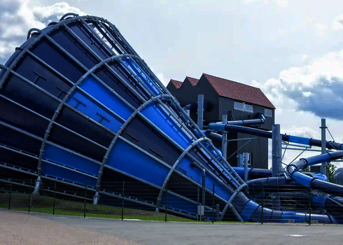 Großer Cyclone-Trichter in Blau mit angrenzender Röhrenrutsche vor modernem Rutschenturm.