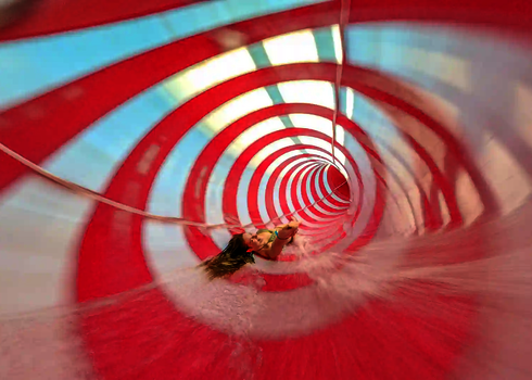 Innenansicht einer Wasserrutsche mit einer rutschenden Frau und gestreiften Tageslichteffekten.