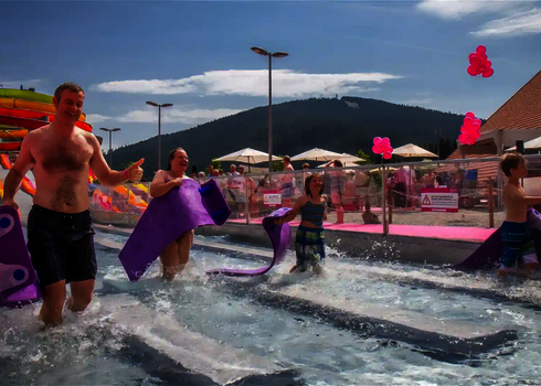 Family leaving the landing area of a water slide at an outdoor pool with slide mats.