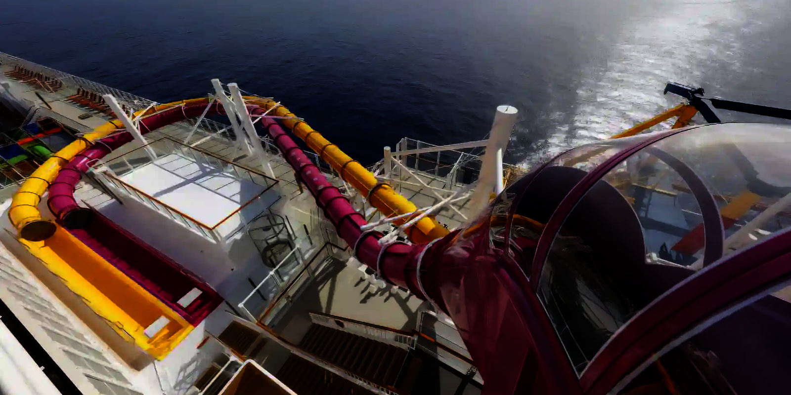 Blick aus der Vogelperspektive auf den Startbereich und den weiteren Rutschverlauf einer pinken und gelben Wasserrutsche auf einem Kreuzfahrtschiff.