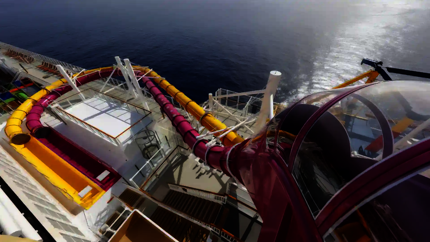 Blick aus der Vogelperspektive auf den Startbereich und den weiteren Rutschverlauf einer pinken und gelben Wasserrutsche auf einem Kreuzfahrtschiff.