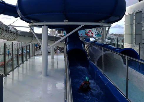 Kind mit Badekappe rutscht aus einer blauen Röhrenrutsche und kommt in einem Auslaufbecken an.