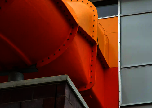 Orangefarbene Wasserrutsche tritt seitlich aus einer modernen Gebäudefassade heraus.