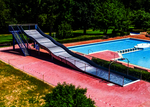 Eine Breitwellenrutsche mit Auslaufbecken und Treppenaufgang, im Hintergrund ein blaues Schimmbecken.