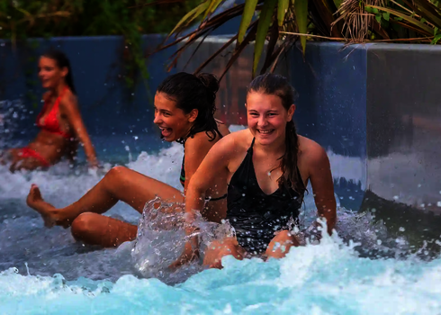 Zwei Mädchen rutschen nebeneinander durch den Wildwasserfluss und lachen.