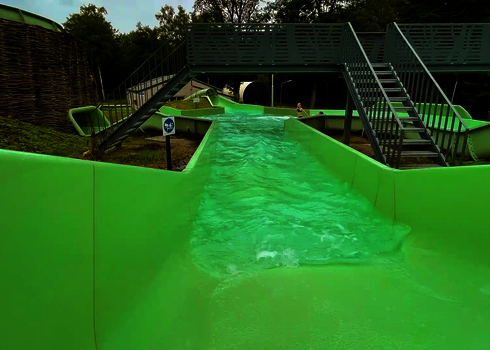 Blick von oben auf Wasserrutsche mit leichter Strömung, im Hintergrund eine Brücke mit Treppenaufgang.