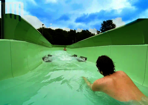 Zwei Personen rutschen nacheinander bäuchlings durch den grünen Wildwasserfluss.