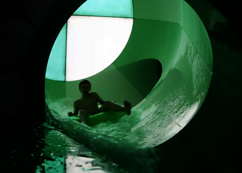 Ein Junge rutscht im grünen Reifen durch den grün-weißen Crazy Cone Tunnel.