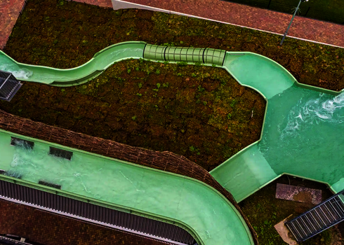 Grüner Wildwasserfluss mit Wasserauslass in ein blaues Auffangbecken auf Dachhöhe.