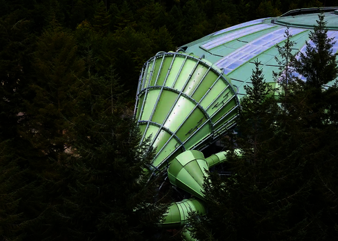 Teilweise verdeckter Cyclone-Trichter in Grün, von Bäumen umgeben, an großes Gebäude angeschlossen.