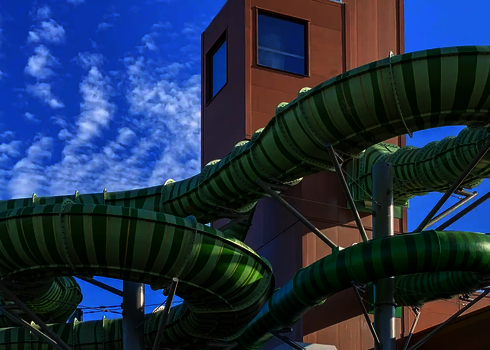 Grüne Family Twister Wasserrutsche mit Stahlkonstruktion vor modernem Gebäude.