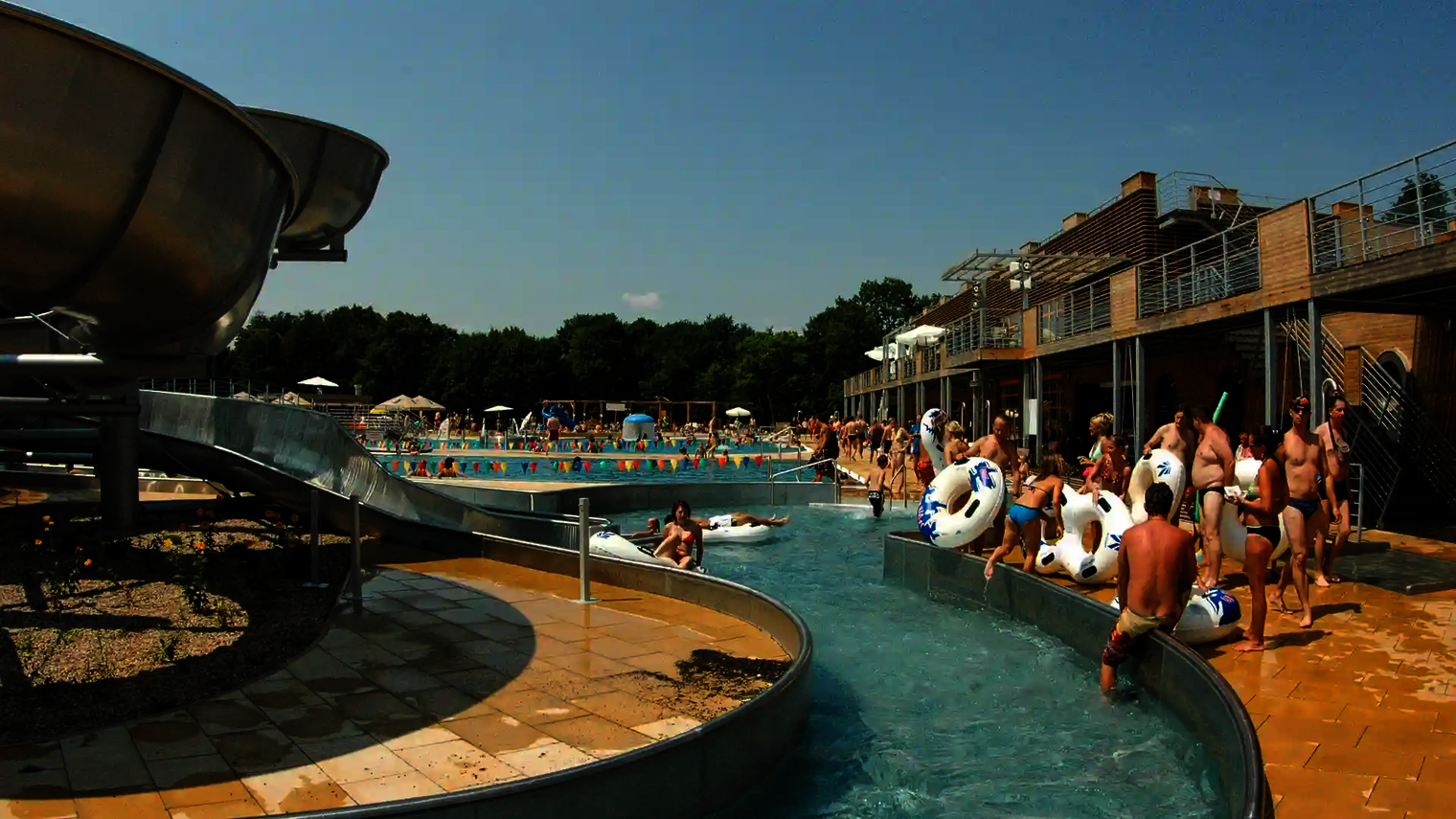 Schwimmbad mit mehreren Badegästen, die sich innerhalb und außerhalb des Lazy Rivers befinden.