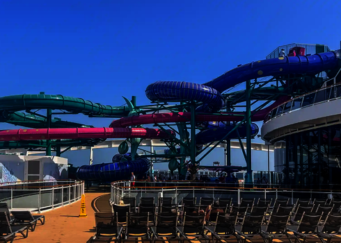 Blick auf eine riesige, bunte Rutschenanlage auf einen Kreuzfahrtschiff, im Vordergrund Stühle.
