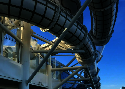 Teiltransparente Wasserrutsche mit grünem Rastermuster unter blauem Himmel.