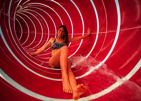 Innenansicht einer pinken Röhrenrutsche, in der eine Frau rutscht, umgeben von Lichtspielen.