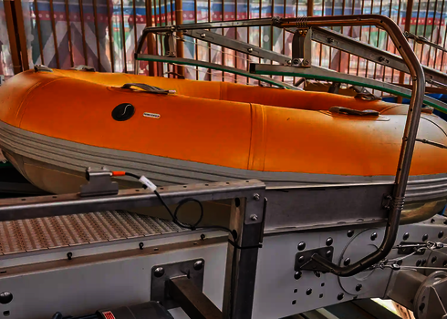 Close-up of a yellow slide raft on the side-guided conveyor belt of the raft conveyor.