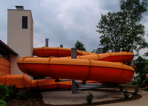Die Reifenrutsche Family Twister schlängelt sich in mehreren orangefarbenen Kurven durch eine Außenanlage.