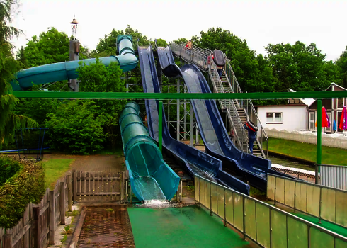 Blick auf mehrere blaue Rutschen in parkähnlicher grüner Umgebung.