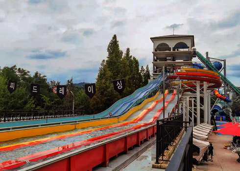 Matracer Wasserrutsche mit bunten Bahnen, an der Seite Sitzmöglichkeiten.