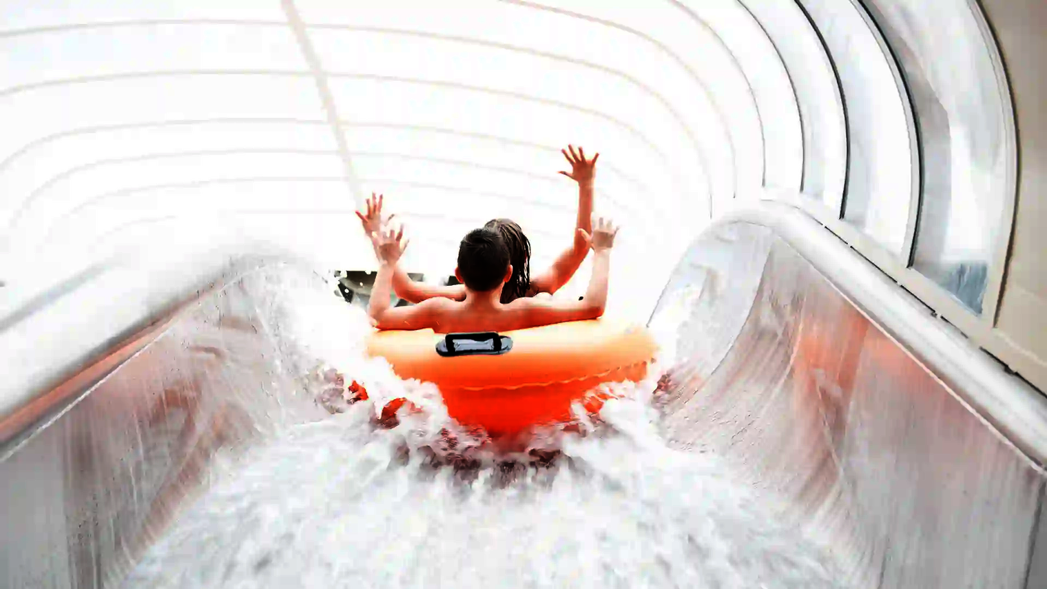 Kinder fahren in orangem Doppelreifen durch die transparente Röhre des Raft Racer.
